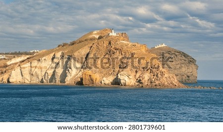 Volcanic cliffs and layered rock formations on Santorini island with a small chapel overlooking the Aegean Sea.