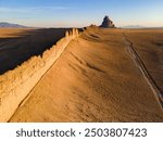 Volcanic rock wall leads to Shiprock New Mexico at sunrise with long shadows