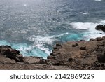 A volcanic rocky shoreline contrasted against varying shades of blue of the Pacific Ocean in Wailuku, Maui, Hawaii, USA