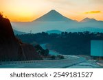 Volcano called "Agua" at sunset in Guatemala Central America, silhouette of mountains and modern highway, dramatic landscape on the road, play of light and shadow.