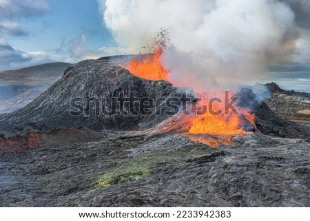 Volcano eruption in Iceland. active volcano with lava fountain. Lateral outflow of the hot reddish lava. View of volcano in the day with sunshine. clouds in the blue sky