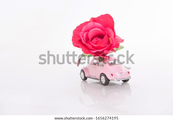 Volkswagen, Moscow, 10.02.2020: pink toy car carries\
a red rose. toys and decorations on a white background. Concept of\
international women\'s day, happy birthday,Valentine\'s Day, flower\
delivery. copy