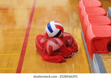 Volleyballs stored after practice in a red net on a gym floor - Powered by Shutterstock