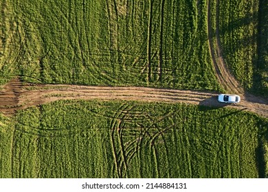 Vologda Region, Russia - May 2018: 
 Top view of the dirty road - the path on the background of green grass and meadows. Aerial photo and abstract texture background. White car rides