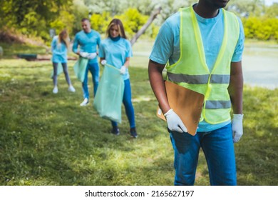 Volontaire Walking With A Group Of Friends In The Park, Wearing Blue Shirts. They Are Part Of A Team Of Volunteers Working On A Community Service Project.

