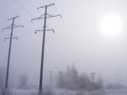 Voltage Line. The Poles On The Field In Misty Weather. Power Infrastructure During Winter. Fog Conditions With A Little Bit Of Snow.