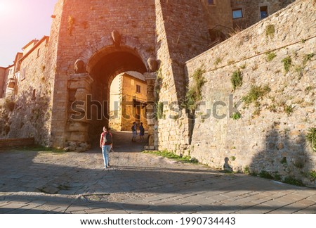 Volterra, Tuscany, Italy. Etruscan gateway to the medieval village. A woman stopped to watch the sunset, two boys are under the arch.