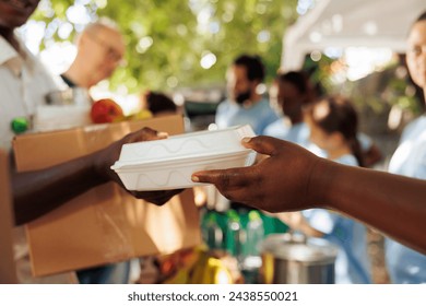 Volunteer of african american descent offers warm meal to an impoverished and hungry individual. Photo focus on the less fortunate person receiving complimentary food from charitable worker.