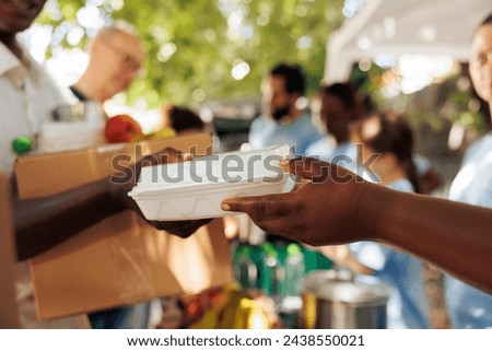 Volunteer of african american descent offers warm meal to an impoverished and hungry individual. Photo focus on the less fortunate person receiving complimentary food from charitable worker.