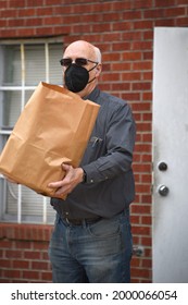 Volunteer Brings Out Grocery Bag Of Food To Customers At A Local Food Bank.  He Is Wearing A Mask For His Protection And Theirs.