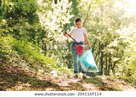 Volunteer cleaning up the forest, she is collecting trash and holding a garbage bag, environmental protection concept