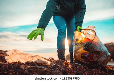 A volunteer collects garbage on a muddy beach. Close-up. The concept of Earth Day. Bottom view. - Shutterstock ID 1923099980