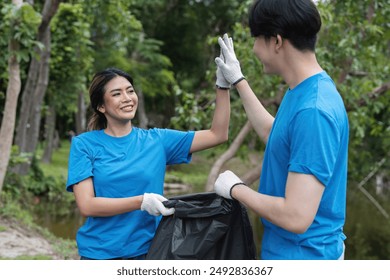 Volunteer Couple Collecting Trash in Park, Environmental Cleanup, Teamwork, Community Service, Eco-Friendly Activity, Smiling, High-Five, Blue Shirts, Gloves, Nature Background - Powered by Shutterstock