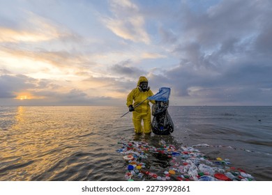 Volunteer ecologist in yellow protective suit and gas mask collects ocean plastic pollution at sunset Symbol of environmental awareness ocean cleaning marine debris protection and climate action - Powered by Shutterstock