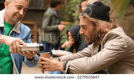 Volunteer giving drink to homeless man outdoors