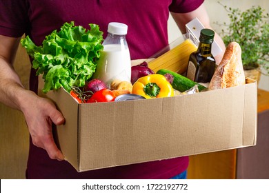 Volunteer Holding Food In A Donation Cardboard Box With Various Food. Open Cardboard Box With Oil, Vegetables, Milk, Canned Food, Cereals And Pasta. Food Delivery Concept With Copy Space.