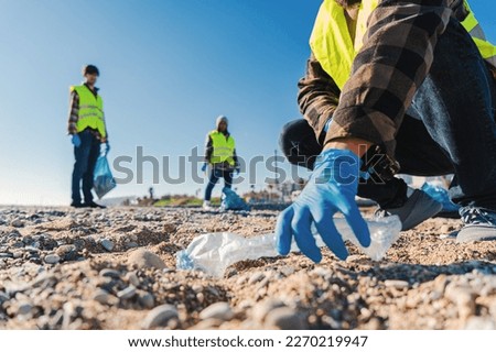 Volunteer man's hand with gloves picking up plastic rubbish from the beach to clean the sand together with his fellow activists Recycling concept. High quality photo