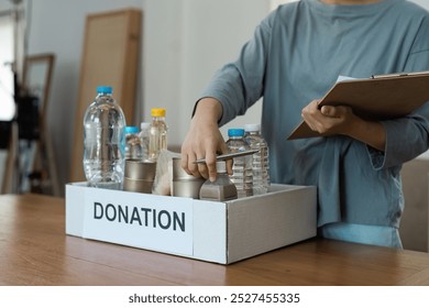 Volunteer Organizing Donation Box with Food and Water Bottles for Charity and Community Support - Powered by Shutterstock