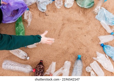 Volunteer Picking Up A Garbage. Frame From Plastic Dirty Bottles With Copy Space On A Sandy Beach. Top View. The Concept Of Environmental Protection And Ecology Template.