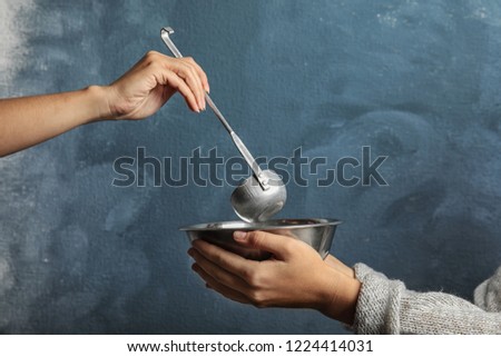 Volunteer putting food into bowl of poor woman on color background, closeup. Concept of help
