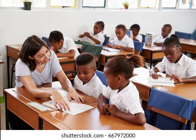 Volunteer Teacher Helping School Kids At Their Desks