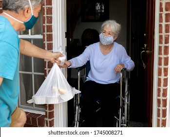 A Volunteer Wearing A Mask Brings Food Donation To An Elderly Handicapped Woman In A Wheelchair During COVID19.