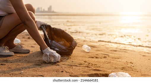 Volunteer woman picking plastic bottle into trash plastic bag black for cleaning the beach, female clean up garbage at sunset, Ecology concept and World Environment Day, Save earth concept