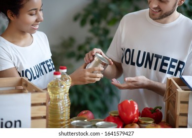 Volunteer Work. Young Girl And Man Standing At The Table And Packing Free Food In Wooden Boxes For The Needy, Smiling Busy.