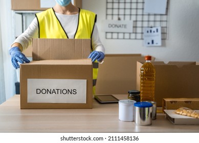 Volunteer Working At Charity Community Service Collecting Food Wearing Protective Masks - Focus On Left Glove Holding Box