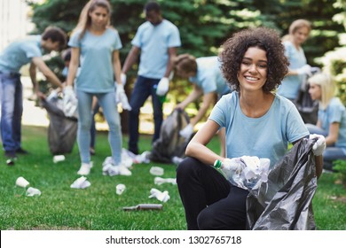 Volunteering, charity and clean environment concept. Happy black woman and group of volunteers with garbage bags cleaning area in park, copy space