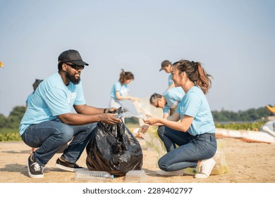 volunteering, charity, cleaning, people and ecology concept - group of happy volunteers with garbage bags cleaning area on sandy shore. - Powered by Shutterstock