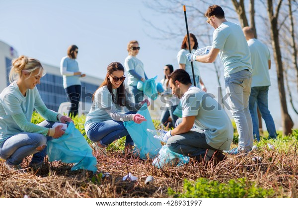 volunteering, charity, cleaning, people and ecology\
concept - group of happy volunteers with garbage bags cleaning area\
in park