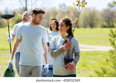 volunteering, charity, people and ecology concept - group of happy volunteers with tree seedlings and rake walking in park - Powered by Shutterstock