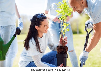 volunteering, charity, people and ecology concept - group of happy volunteers planting tree and digging hole with shovel in park - Powered by Shutterstock