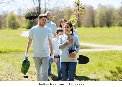 volunteering, charity, people and ecology concept - group of happy volunteers with tree seedlings and rake walking in park - Powered by Shutterstock