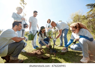 Volunteering, Charity, People And Ecology Concept - Group Of Happy Volunteers Planting Tree And Digging Hole With Shovel In Park