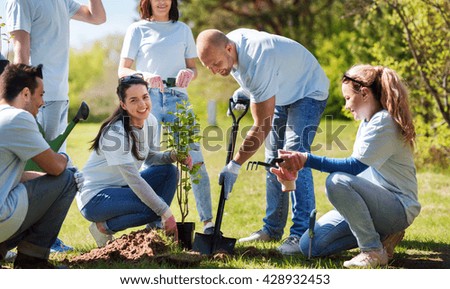 volunteering, charity, people and ecology concept - group of happy volunteers planting tree and digging hole with shovel in park