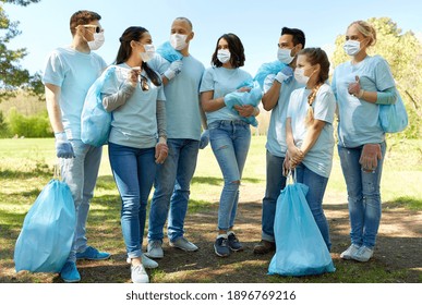 volunteering, health and ecology concept - group of volunteers wearing face protective medical mask for protection from virus disease with garbage bags talking in park