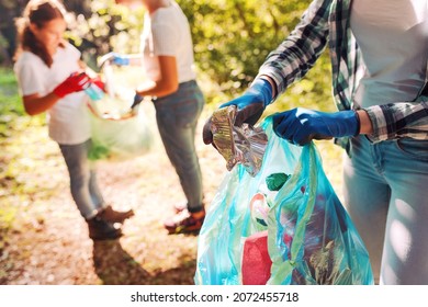 Volunteers cleaning up the park, a woman is putting trash in a garbage bag and some kids are helping her, environmental protection concept - Shutterstock ID 2072455718
