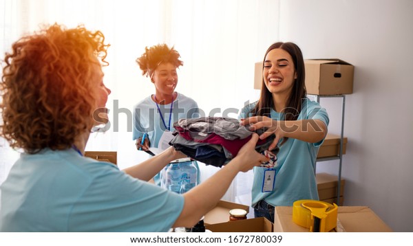 Volunteers Collecting Food Donations In\
Warehouse. Team of volunteers holding donations boxes in a large\
warehouse. Volunteers putting clothes in donation boxes, social\
worker making notes\
charity