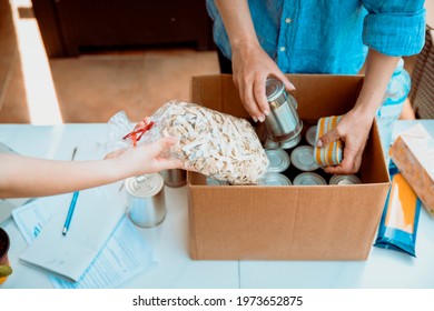 Volunteers Collecting Food Into Donation Box. Working At Food Bank Concept. Cut Out Middle Section Image Of Hands Packing Cans At Food Drive.