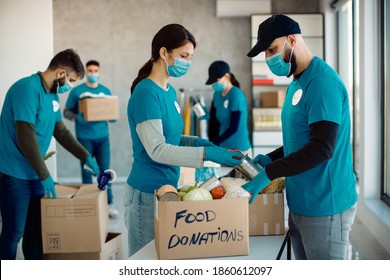 Volunteers Cooperating While Sorting Food In Donation Boxes For Charity Food Bank.