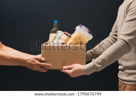 Volunteers with donation box with foodstuffs on dark background