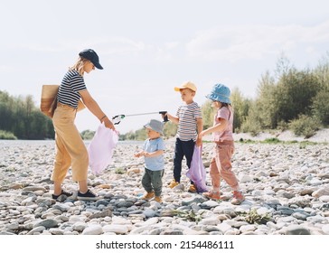 Volunteers Family Collecting Plastic Waste Trash On River Beach. People Help To Keep Nature Clean Up And Pick Up Garbage. Woman And Kids Helping Clean Up Outdoor Area From Rubbish.