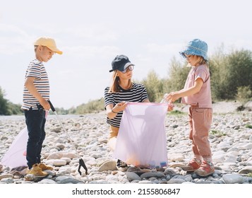 Volunteers Family Collecting Plastic Waste Trash On River Beach. People Help To Keep Nature Clean Up And Pick Up Garbage. Woman And Kids Helping Clean Up Outdoor Area From Rubbish.