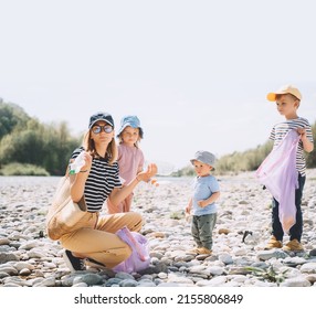 Volunteers Family Collecting Plastic Waste Trash On River Beach. People Help To Keep Nature Clean Up And Pick Up Garbage. Woman And Kids Helping Clean Up Outdoor Area From Rubbish.