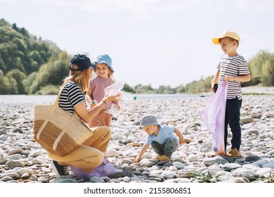 Volunteers Family Collecting Plastic Waste Trash On River Beach. People Help To Keep Nature Clean Up And Pick Up Garbage. Woman And Kids Helping Clean Up Outdoor Area From Rubbish.