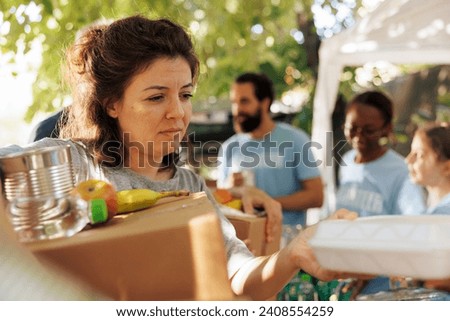 Volunteers hand out packages and meal boxes offering free food to the homeless and needy. Close-up of underprivileged caucasian woman receiving hunger relief donation package from charity workers.