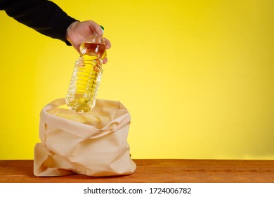 The Volunteer's Hands Put A Bottle Of Vegetable Oil In A Donation Bag. Assistance To Elderly People During Quarantine Due To Coronavirus Covid 19. Food Delivery