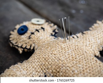 A voodoo doll made of burlap, with buttons for eyes, pierced with many needles right through the heart, close-up. The concept of unrequited love, revenge on a person for cheating or causing pain.